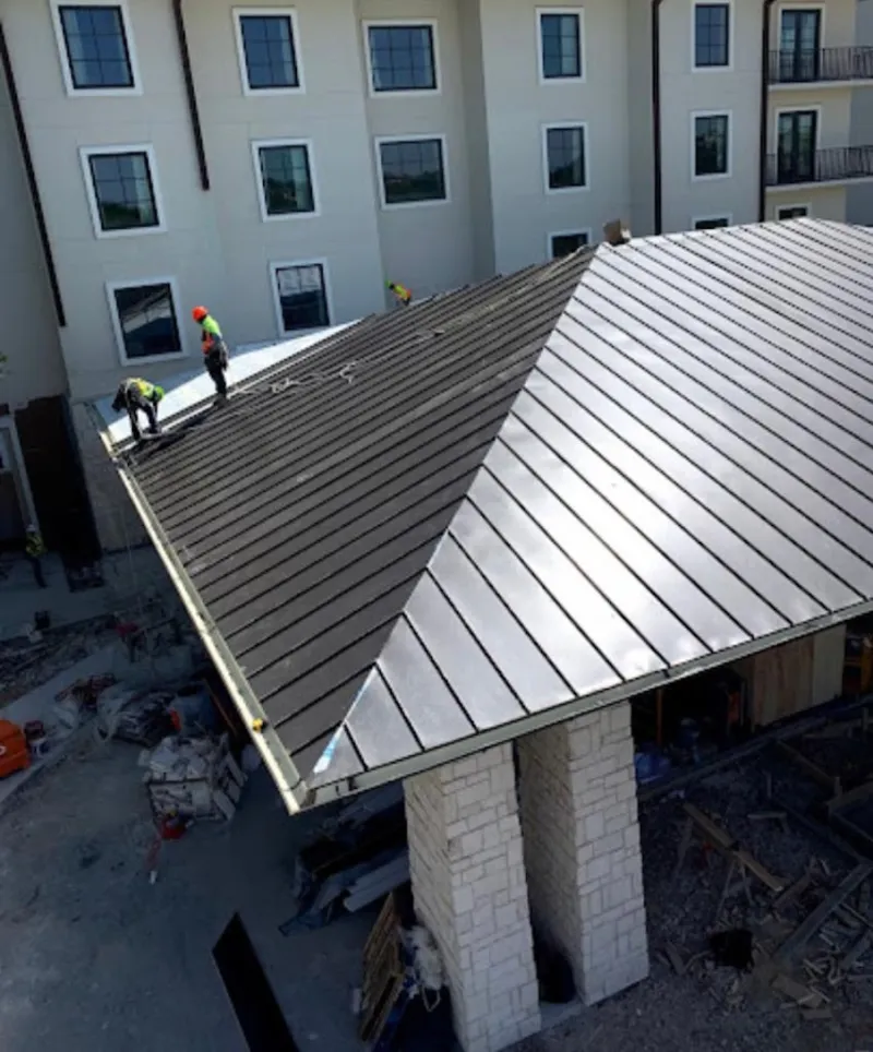 Crew installing standing seam metal roof panels on a commercial project in Lee